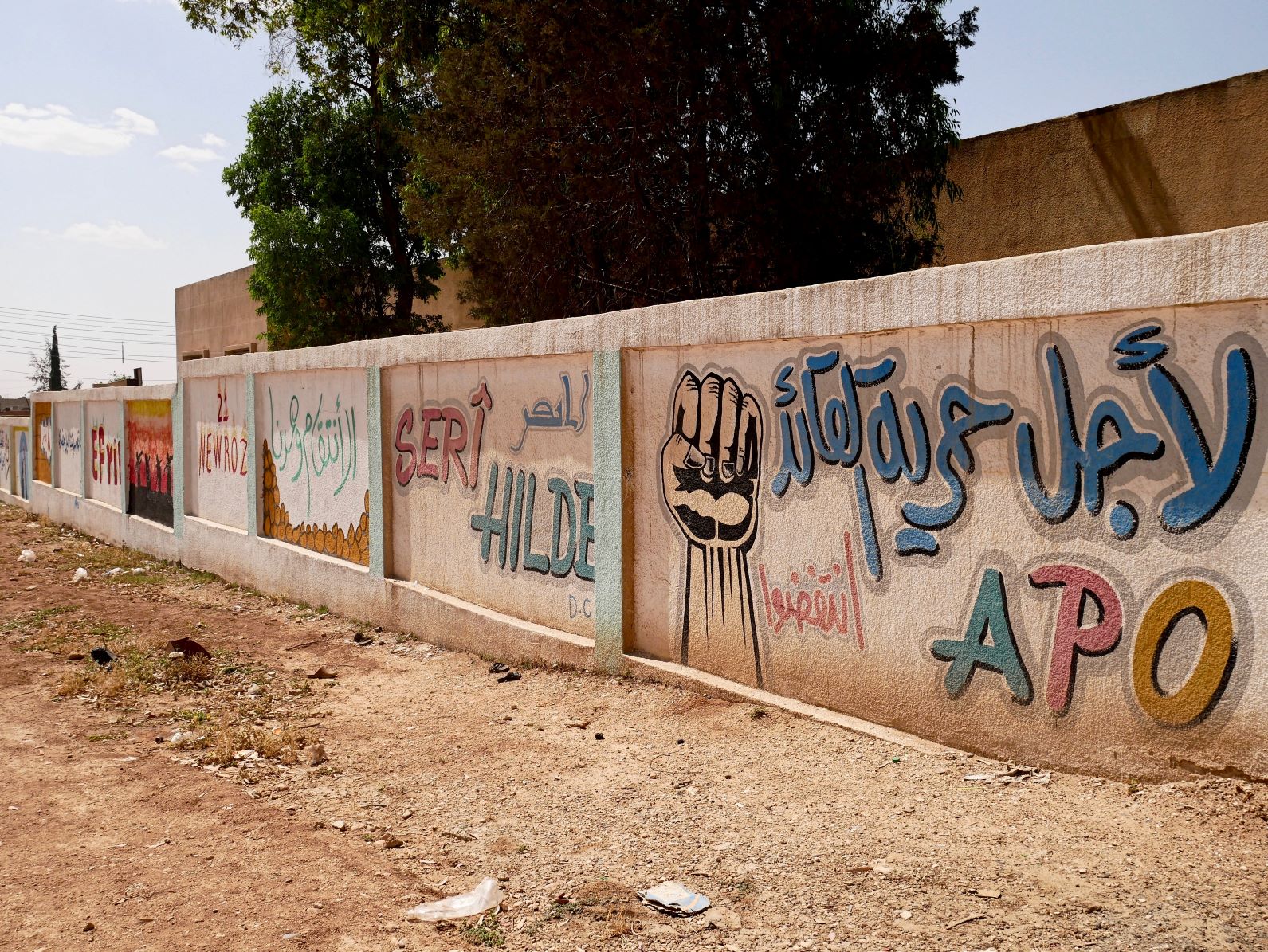 Pinturas en una pared que rodea una escuela en Qamişlo, Rojava, que significan la libertad con la que los kurdos ahora pueden celebrar su identidad allí. Las pinturas incluyen 'Apo', un apodo para Ocalan, 'Newroz', o año nuevo kurdo, cuya celebración fue prohibida en Siria y Turquía, y 'Efrin', que Turquía capturó en marzo de 2018. Foto por Elise Boyle Espinosa, 2018. 